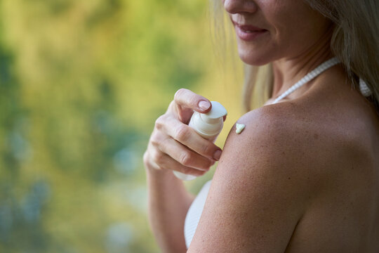 Portrait of a woman applying skin care cream outdoors in summer