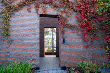 Architecture entrance framed by brick and foliage with minimalism shaped by shadow and sunlight, bringing geometry, structure and contrast into a clean contemporary scene