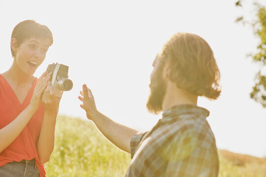 Woman holding 8mm camera and filming man in field