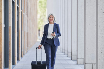 Businesswoman in a suit walking with luggage outdoors at a trade fair
