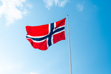 Norwegian flag waving on flagpole against blue sky outdoors