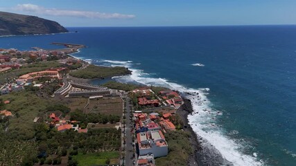 High altitude aerial drone approach shot flying over the vast Atlantic Ocean towards the colorful hillside town and port of Vueltas, Valle Gran Rey, La Gomera. - Powered by Adobe