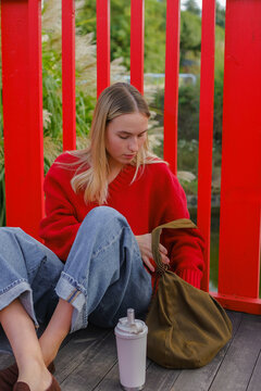 Young woman in red sweater journaling outdoors with drink, slow living