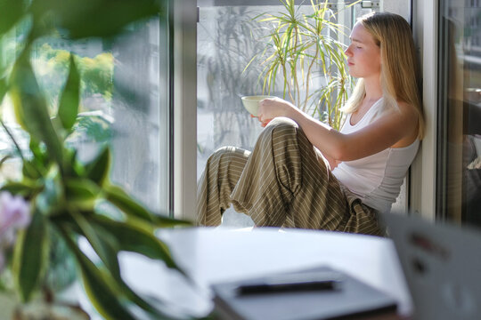 Woman enjoying coffee break by window while working remotely at home