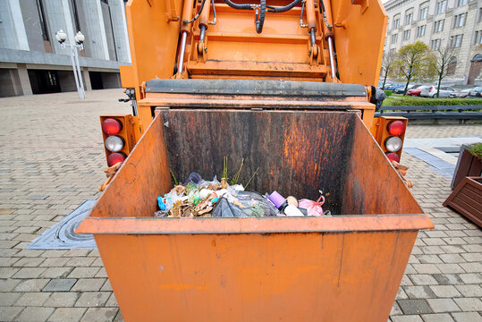 Heavy-duty orange hydraulic garbage truck parked on the city square during routine waste pickup operation, remove trash and maintain cleanliness within busy urban streets. Hydraulic garbage compactor