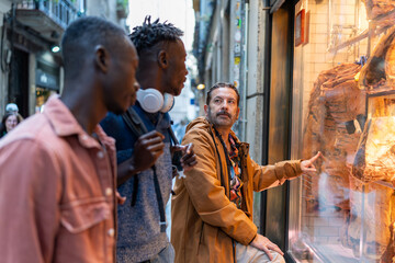 Group of multi-ethnic male friends looking at dry-aged steaks in a premium delicatessen window...
