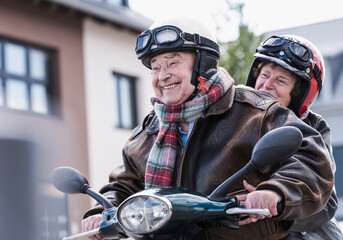 Happy senior couple riding scooter outdoors in urban area