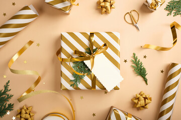 Christmas golden and white present with empty gift tag on beige background. Items for wrapping. Copy space