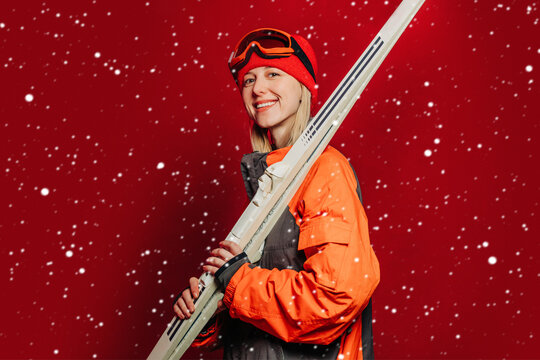 Smiling skier in orange suit with skis and goggles on red background