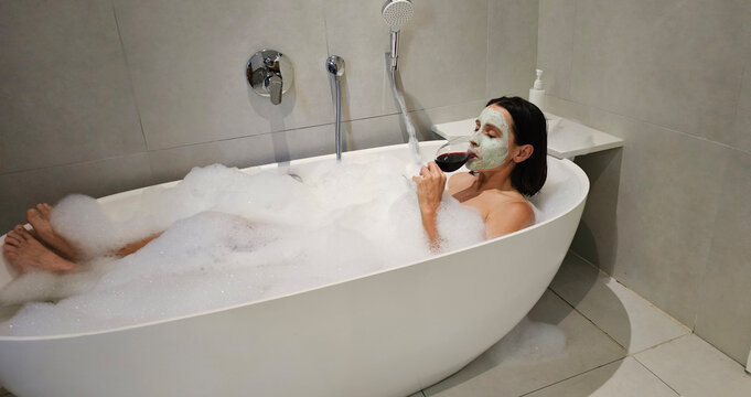 woman relaxing in a bubble bath, enjoying a glass of wine