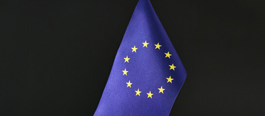 A person is holding a small European Union flag in front of a black background concept