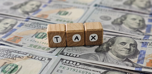 spelling the letters tax top of several US hundred dollar bills concept