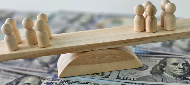 wooden seesaw balanced on top of a stack of US dollar bills concept