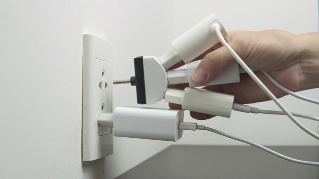 Hand inserting electrical plugs into outlet. Electrical overload