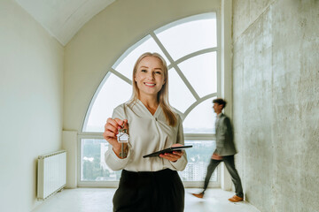 Realtor holding key in modern apartment with client in background
