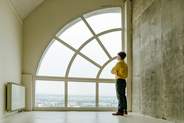 Thoughtful businessman looking out large window in modern urban loft