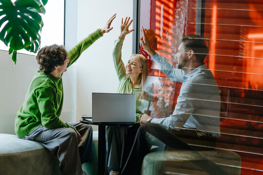 Colleagues celebrating teamwork achievement with high five in office