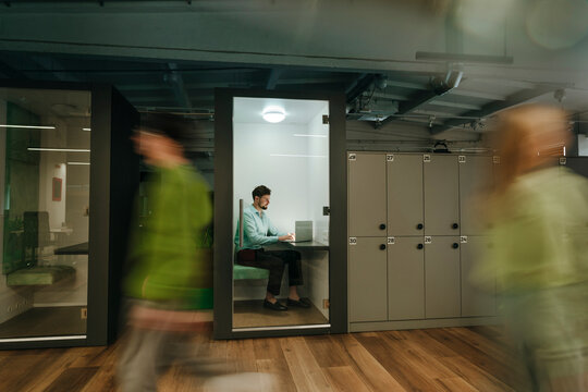 Businessman working on laptop in modern office cubicle with motion blur