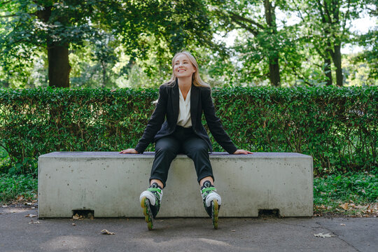 Woman in business wear smiling on bench with roller skates outdoors