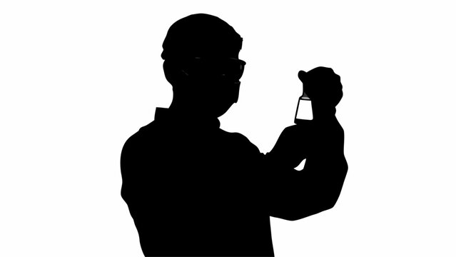 Silhouette of person wearing glasses and mask holding a small bottle up to the light to examine it