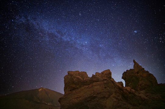 View of rock formations Roques de Garcia, the Milky Way galaxy and Teide mountain volcano, Teide National Park, Tenerife, Spain. Astrophotography of night sky. Long time exposure night landscape.