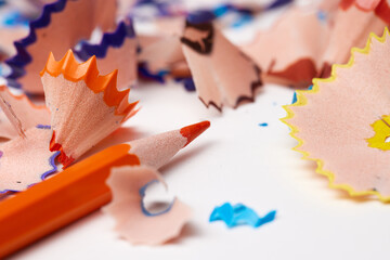 Orange pencil tip surrounded by colorful wood shavings on a white background