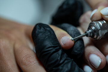 Professional manicurist cleaning cuticles with a rounded electric tool during nail care session