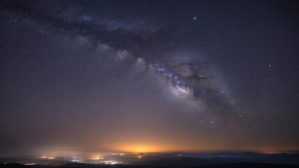 Night sky with milky way and city lights glowing on the horizon below