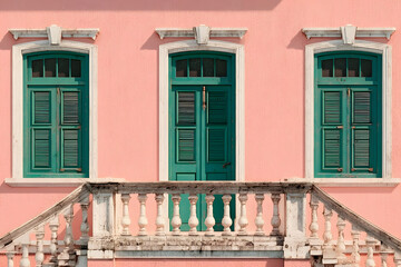 Naklejka premium Vintage architecture with green shutters on a pink wall, featuring a classic balustrade