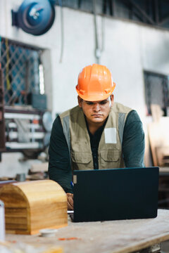 Successful worker using a computer in the carpentry workshop. Carpenter using a laptop at a workbench in the workshop