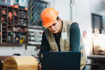 Carpenter using a laptop at a workbench in the workshop. Successful worker using a computer in the carpentry workshop