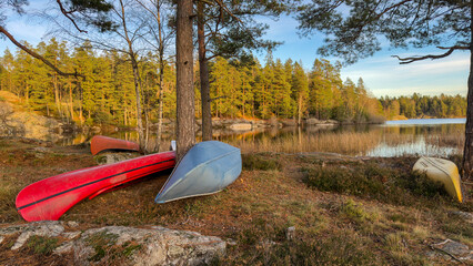Beautiful view of the lake shore in autumn. Colorful kayaks and boats lie on the shore. A tranquil autumn lake landscape with perfect tree reflections. Recreation tourism hiking in the fall season.