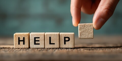 Wooden blocks spelling the word help with a hand placing a blank block on a wooden surface