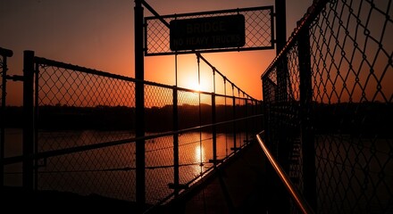 Dramatic Sunset Glow Illuminated Over Chain Link Bridge Against Fiery Orange Sky