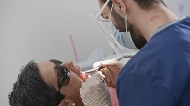 Professional male dentist carrying out dental treatment on patient with specialized tools in clean modern clinic environment
