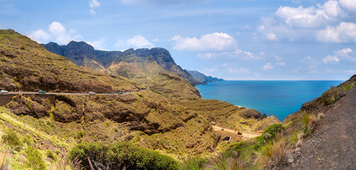 Obraz premium Guayedra, Agaete, Gran Canaria, GC-200 – wide panoramic view along the winding coastal road above the steep cliffs, blue Atlantic and summer sky.