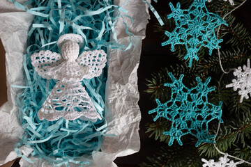 Handcrafted white crochet angel nestled in a gift box with blue filler, surrounded by fir branches and delicate blue crochet snowflakes. Festive handmade décor perfect for winter and holiday themes.