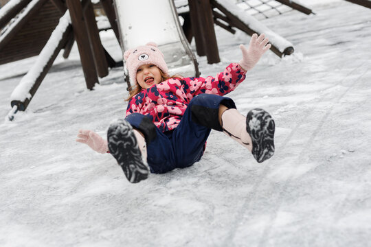 Child sliding down icy playground slide. Happy kid playing outdoors in cold weather