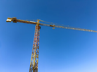High yellow tower crane rising against clear blue sky, captured from low angle within bright daylight