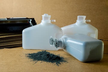Three white toner refill bottles with spilled black powder on a cardboard surface, representing...