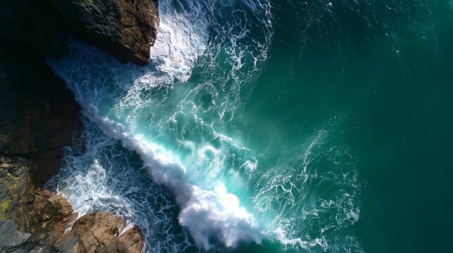 Waves crash against rocky shore creating foam in bright blue ocean water