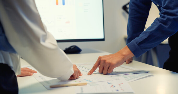 A close-up shot of two business people's hands pointing at financial graphs on paper documents placed on a desk. The image highlights detailed data analysis and collaborative teamwork.