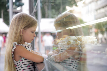 Grumpy and sad little girl looking at a cake store window	