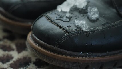 Close-up of melting snow on black leather boots indoors