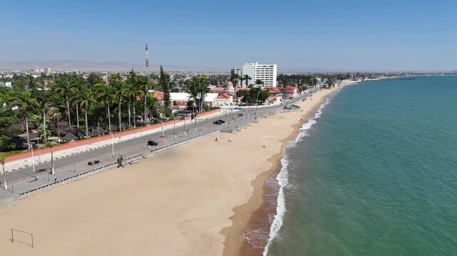Aerial panorama of Benguela city, Angola, showing long sandy coastline, waterfront avenue, and palm trees separating town life from the beach below