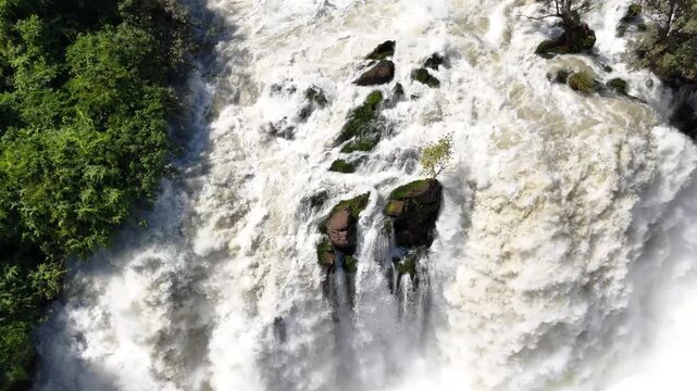 drone footage descending over the roaring Binga Falls in Angola, revealing the immense flow of water plunging through rocky cliffs and dense rainforest