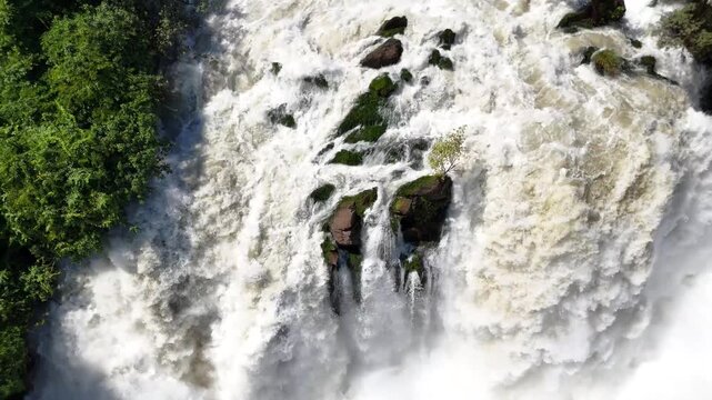 Aerial drone close-up of Binga Falls in Angola, revealing the immense drop of cascading water crashing over rocks into the misty canyon below in a tropical landscape