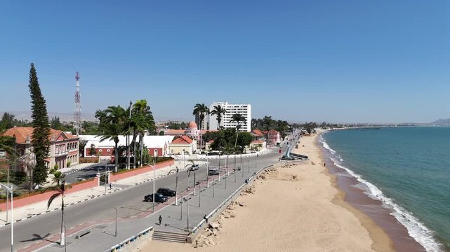Drone footage of Benguela beachfront, Angola, showing palm-lined promenade, colonial buildings, and calm Atlantic Ocean under bright tropical sunlight