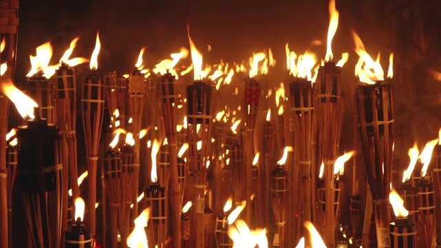 Close-up of a single lit bamboo torch with many others glowing in the blurred background, creating a warm and intense flame-filled atmosphere.