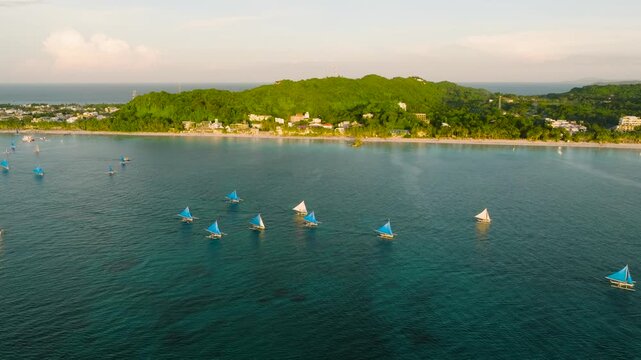 Sailboats on a serene turquoise sea with lush tropical trees lining the coast. Boracay Island, Philippines.